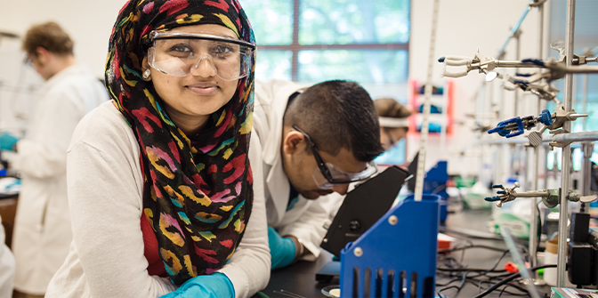 Woman in a computer science lab wearing a hijab and work goggles