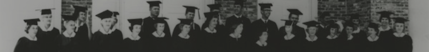 Black and white photo of about 20 people standing in cap and gown